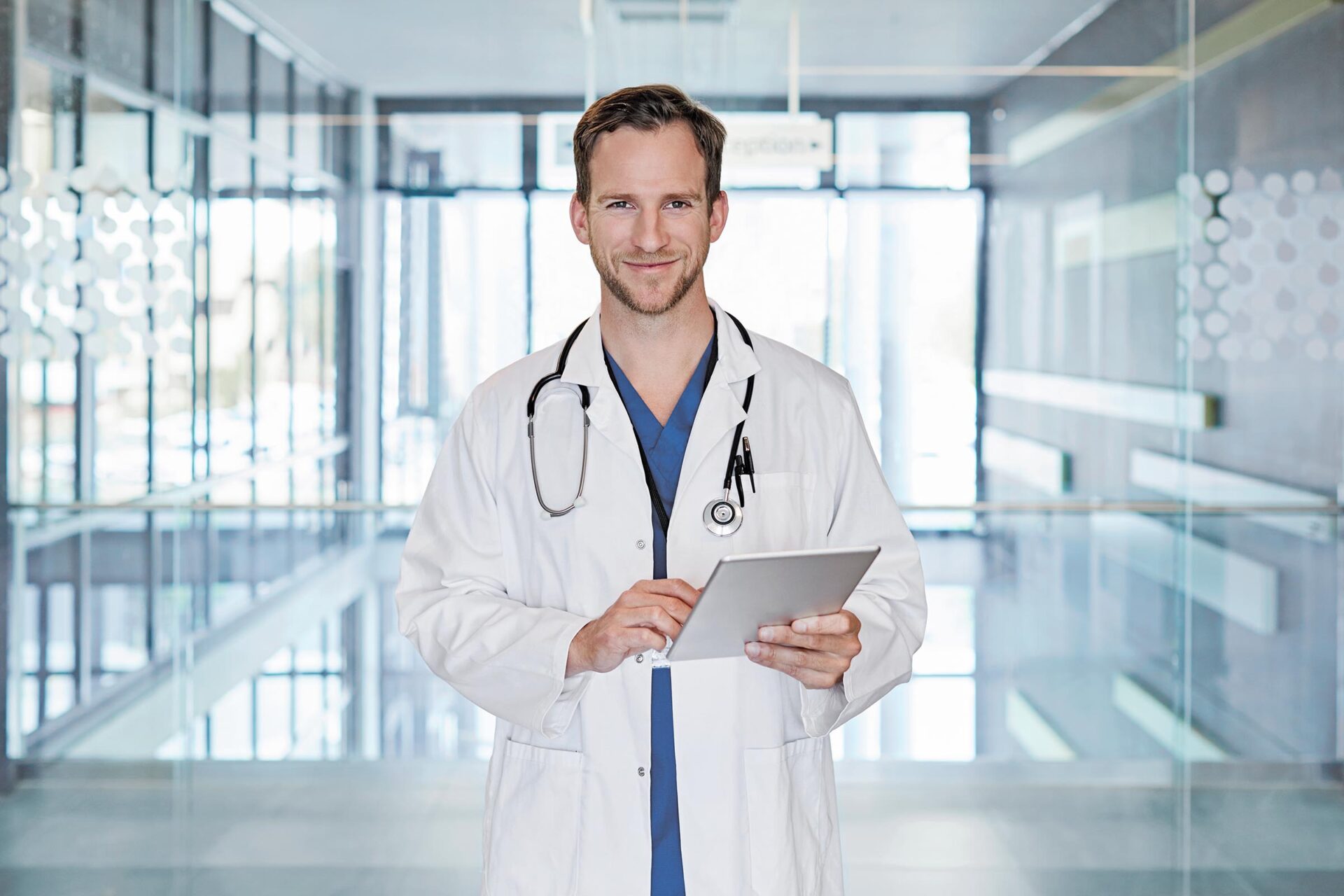 Arzt mit Tablet in der Hand lächelt in einem Krankenhaus.